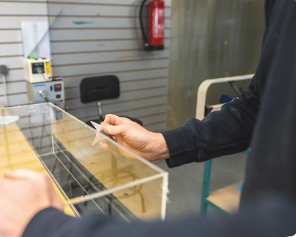 Persoon in werkplaats die een transparante stofkap naloopt met een scraper